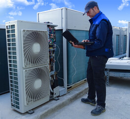 air conditioning technician making a diagnosis of an industrial air conditioning unit with a laptop...