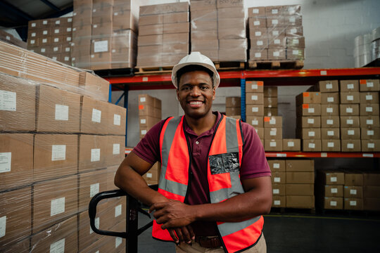 Male factory worker smiling besides packages in warehouse 