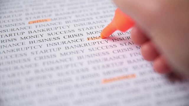 Hand highlight word finance with orange marker on printed text, macro shot. Finance crisis concept