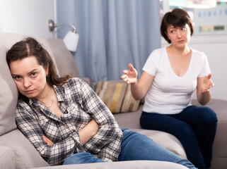 Sad young female and her elderly sister sitting at sofa during quarrel at home