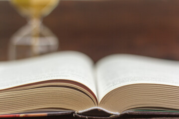 An open hardcover book and an hourglass in the background.