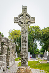 Drogheda, Ireland - July 15, 2020: View of West face of West high celtic cross and round tower at early Christian monastic settlement Monasterboice founded in 5th century. - 387075368