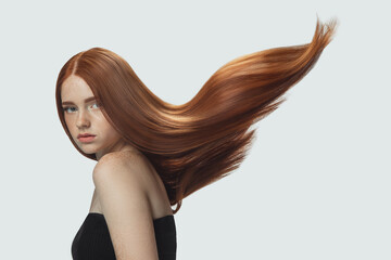 Beautiful model with long smooth, flying red hair isolated on white studio background. Young caucasian girl with well-kept skin and hair blowing on air. Concept of salon care, beauty, fashion.