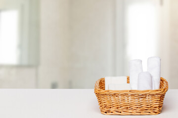 Obraz na płótnie Canvas Basket with bath accessories such as soap bars, Cream and cosmetic tissues for body care on a white table over blurred bath background with copy space. For your product display montage.