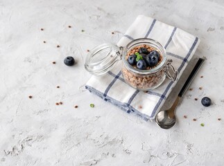 Buckwheat porridge jar. Boiled buckwheat in a glass jar with blueberries and a spoon on a light background with space for text. Top view 