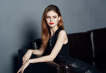 Fototapeta na wymiar Elegant woman in a dark dress on a leather sofa and evening makeup