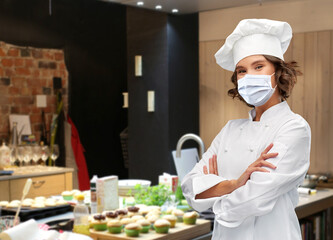 cooking, culinary and health concept - female chef in toque wearing face protective medical mask for protection from virus disease with crossed arms over restaurant kitchen background