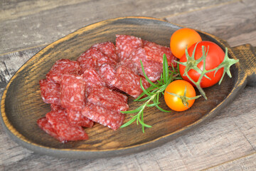 Salami sliced in squares and vegetables on rustic wooden plate.