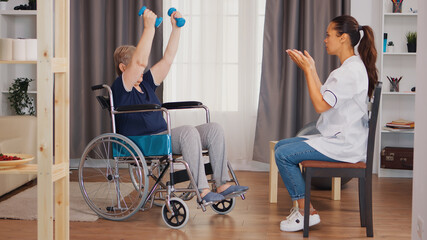 Old lady in wheelchair exercising with dumbbelss. Nurse helping with rehabilitation. Training, sport, recovery and lifting, old person retirement home, healthcare nursing, health support, social