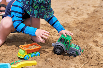A child on the beach plays in the sand with plastic toy cars
