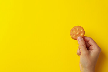 Fototapeta na wymiar Female hand hold cracker biscuit on yellow background