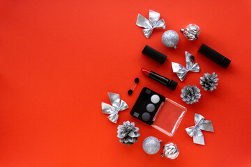 Christmas flat lay of makeup products and decorations. Eyeshadow and lipstick on red background. Space for text