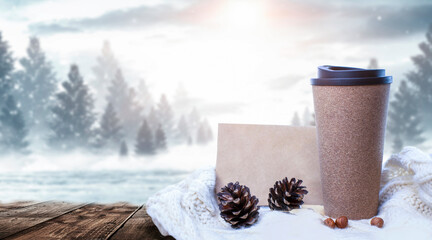 Hot coffee on a wooden table against the background of a winter landscape in a winter snowy forest. Coffee on the background of winter mountains. Snowflakes, frost.