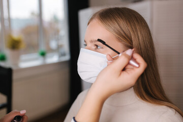 Female makeup artist working in beauty salon during quarantine. Make up artist in medical mask....