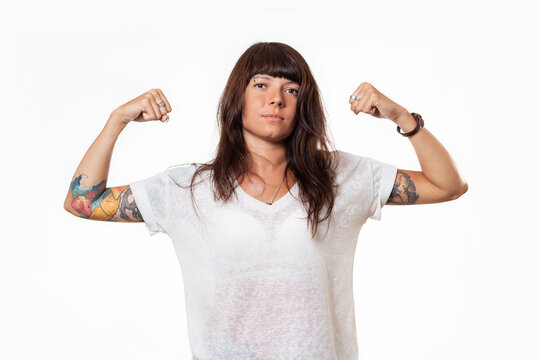 Concept of feminism and equal rights for women. Portrait of caucasian young woman with tattoo who shows her biceps. White background