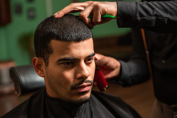 African-American barber's hand uses razor and haircut on Hispanic Latino man with goatee in a...