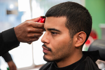African-American barber's hand uses razor and haircut on Hispanic Latino man with goatee in a...