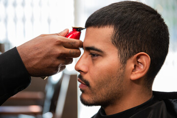 African-American barber's hand uses razor and haircut on Hispanic Latino man with goatee in a...