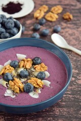 Blueberry smoothie bowl topping with walnut, coconut chips, chia seeds and blueberries. Wooden background