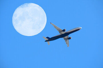 airplane flight against the full moon and blue sky, aviation and travel concept