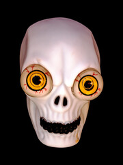 A skull with large eyes and black teeth on a black background.
