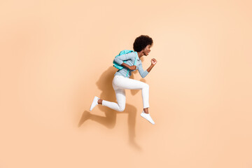 Obraz na płótnie Canvas Photo portrait of black skinned woman hurrying running jumping up with blue rucksack isolated on pastel beige colored background