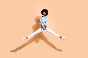 Fototapeta na wymiar Photo portrait of african american woman jumping up holding hands down with spread legs open mouth isolated on pastel beige colored background
