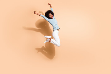 Photo portrait of black skinned girl jumping high up two fists in air cheering screaming isolated on pastel beige colored background