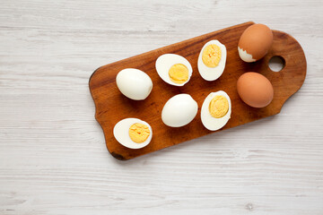 Fototapeta na wymiar Hard Boiled Eggs on a rustic wooden board on a white wooden background, top view. Flat lay, overhead, from above. Copy space.