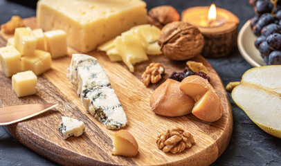 Fototapeta na wymiar Cheese plate from different kind of cheese - Emmental, Homemade, Parmesan, blue cheese, bread sticks, walnuts, raisin, pear, grapes on a table