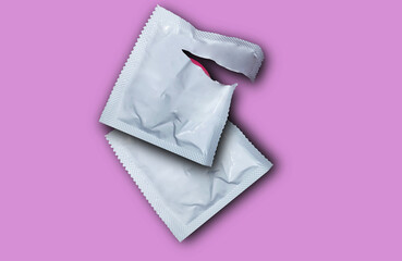 Pink opened condom and condom in pack on a pink background. Safe sex and reproductive health concept.