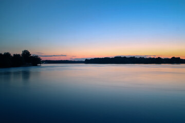 Fototapeta na wymiar Puesta de sol a orillas del río Danubio. Reflejo del cielo colorido en la superficie del agua del delta del Danubio en la localidad de Nufaru, Rumanía.