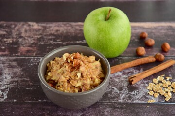 Hot autumn breakfast oat porridge with apple, hazelnuts, honey and cinnamon powder  on a wooden rustic background.