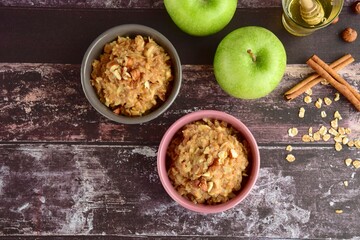 Hot autumn breakfast oat porridge with apple, hazelnuts, honey and cinnamon powder on a wooden rustic background.