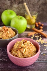 Hot autumn breakfast oat porridge with apple, hazelnuts, honey and cinnamon powder on a wooden rustic background.