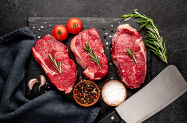 raw three beef steaks on a cutting board with spices on a stone background