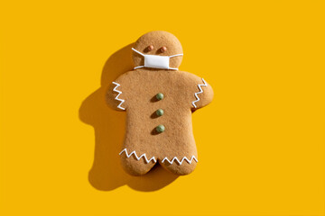 Pandemic Christmas. Celebration restriction. Coronavirus winter holidays protective measures. New normal. Brown gingerbread man in medical face mask alone isolated on orange copy space background.