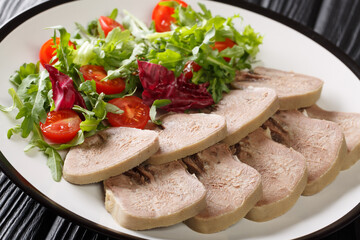 Serving of boiled beef tongue with fresh salad close-up in a plate on the table. horizontal