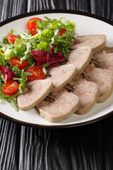 Boiled chopped beef tongue with fresh salad close-up in a plate on the table. vertical