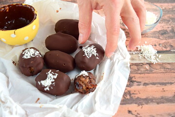 A hand picking dates covered dark chocolate garnish with shredded coconut
