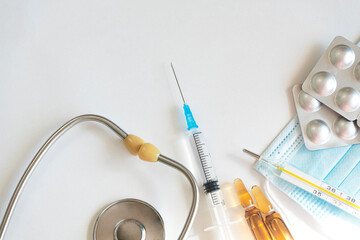 A syringe with a vaccine, ampoules and tablets, a thermometer, a phonendoscope and various medical equipment. Vaccination concept. Copy space. White background, top view