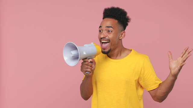 Excited young african american man in yellow t-shirt posing isolated on pastel pink background in studio. People lifestyle concept. Screaming in megaphone pointing index finger aside spreading hands