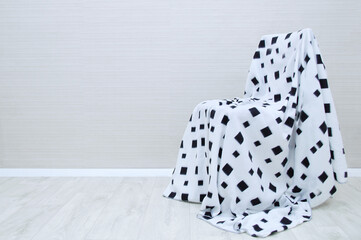 Chair is an armchair with a white blanket draped over in black pattern in the interior of the room.