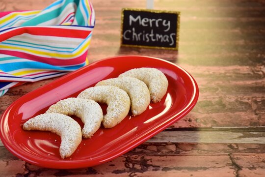 Freshly baked festive German crescent cookies or Vanille Kipferl sprinkled with icing sugar with Merry Christmas written on black board