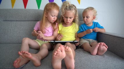 Friendly kids share one tablet computer sitting on sofa. Siblings with tablet pc - Powered by Adobe