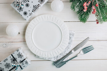Christmas table place setting with empty plate and cutlery on white wooden background