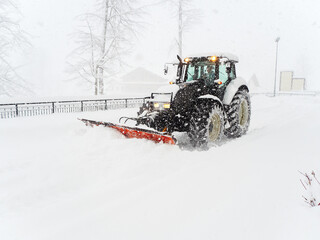 A snow plow tractor clears a snowy road along a fence during a severe blizzard