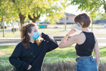 Two young women with face masks greet each other with the elbow, new safe greeting