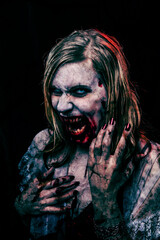 Studio portrait of a female vampire of zombie looking at camera. Black background.