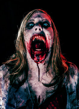 Studio portrait of a female vampire of zombie looking at camera. Black background.